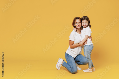 Full length happy woman in basic white t-shirt have fun with cute child baby girl 5-6 years old hold hands. Mom little kid daughter isolated on yellow color background studio Mother's Day love family