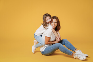 Obraz na płótnie Canvas Full body length happy woman in basic white t-shirt have fun sit on floor child baby girl 5-6 years old Mom mum little kid daughter isolated on yellow color background studio Mother's Day love family.