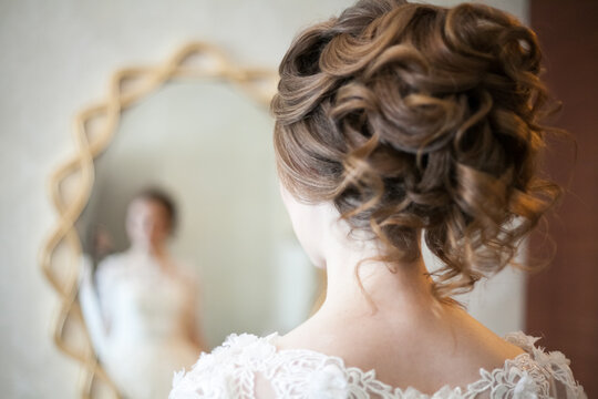 a bride with a beautiful hairstyle looks in the mirror, defocus, curls