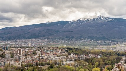 Fototapeta na wymiar Aerial view of urban landscape with many administrative and residential buildings, green park and mountain background, cloudy sky. Sofia, the capital city of Bulgaria, East Europe. Panoramic sight.