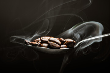 Hot roasted coffee beans on a spoon with aromatic smoke isolated on black background
