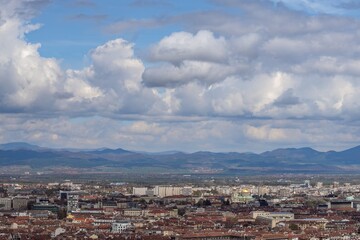 Fototapeta premium Aerial view of urban landscape with many administrative and residential buildings and grey clouds on blue sky background. Sofia, the capital city of Bulgaria, East Europe. Panoramic natural sight.