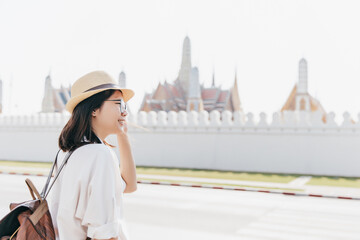 Tourist woman in white shirt and straw hat with brown backpack at Wat Phra Kaew or Grand Palace Temple, Bangkok, Thailand