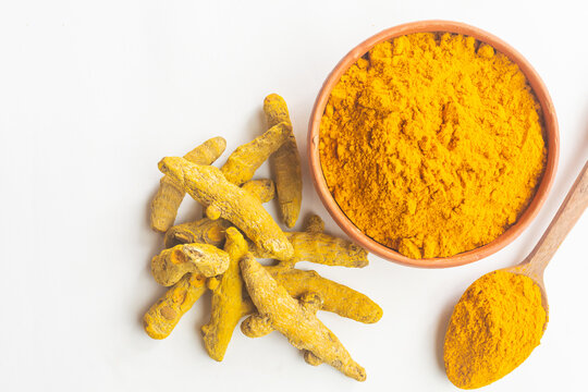 Dry turmeric or haldi powder in a earthen bowl with turmeric roots on white isolated background.