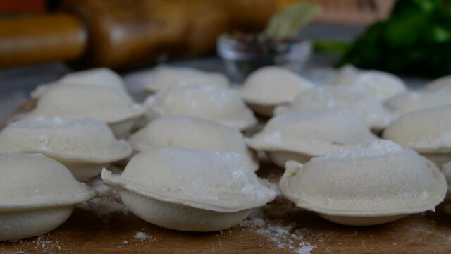 Rows of frozen raw pelmeni dumplings stuffed with mince meat on cutting board. Delicious traditional handmade food on domestic kitchen. Asian and russian cuisine. Dolly shot. Close-up.