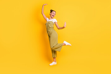 Full size profile photo of optimistic brunette lady dance wear bright t-shirt overall sneakers isolated on yellow color background