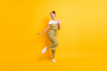 Fototapeta na wymiar Photo of funny carefree lady dance look side open mouth wear green overall shoes isolated yellow background