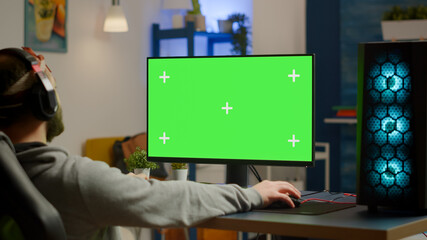 Pro gamer streaming video games with green screen mock-up display in gaming home studio. Player using RGB professional computer with chroma key isolated desktop playing shooter games wearing headset © DC Studio