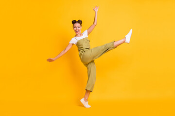 Fototapeta na wymiar Photo of funny adorable lady dance open mouth raise leg wear green overall shoes isolated yellow background
