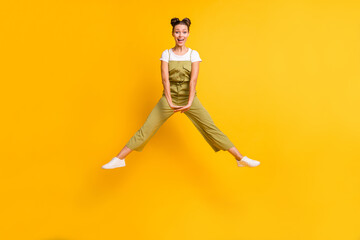 Photo of crazy girlish lady jump hold hands open mouth wear green overall shoes isolated yellow background