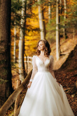 Fototapeta premium Pretty bride with wavy hair walks on a trail in autumn park.