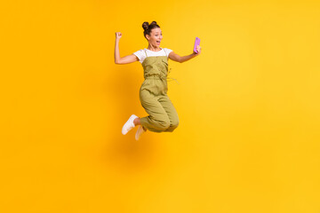 Photo of crazy lady jump hold telephone raise fist open mouth wear green overall shoes isolated...