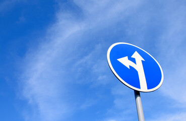 road sign go straight and left on the background of a blue sky with dead clouds