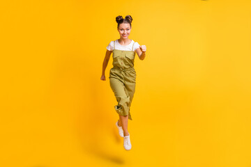 Fototapeta na wymiar Photo of funny positive lady jump run look camera wear green overall footwear isolated yellow background
