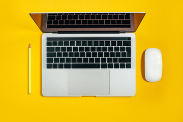Fototapeta na wymiar top view of a laptop next to a white mouse and pencil on a yellow background