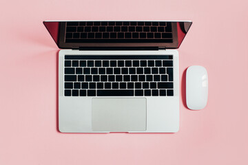 top view of a laptop next to a white mouse and pencil on a pink background