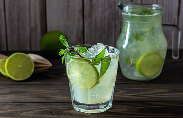 Homemade lemonade with lime, mint in a glass with a jug on a wooden rustic table. Summer refreshing drink.