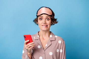 Photo of young attractive sad upset girl bite lips wear eye mask and pajamas using smartphone...
