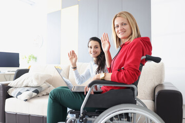 Woman in wheelchair sitting with laptop and waving hand