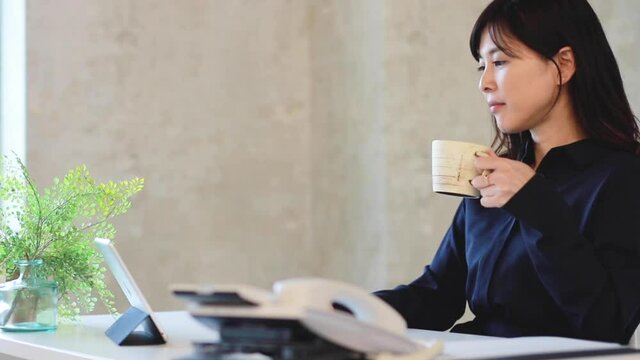 コーヒーを飲みながらタブレットPCを見るビジネスウーマン