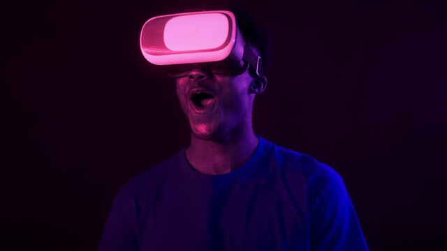Virtual reality fun. Emotional african american guy wearing VR headset enjoying augmented reality in neon lights