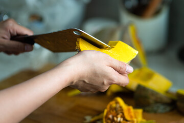 Cooking chef is using a knife to peeling and slicing pumpkin piece, food preparation action photo. Selective focus at human hand that holding the pumpkin.