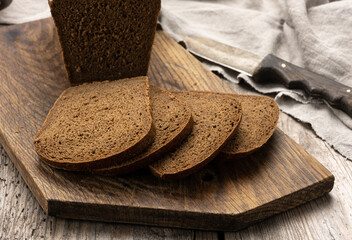 sliced baked rectangular rye flour bread on brown board, healthy food