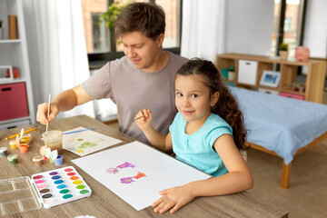 Obraz premium family, motherhood and leisure concept - happy smiling father spending time with his little daughter and drawing with colors at home