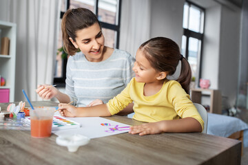 family, motherhood and leisure concept - mother spending time with her little daughter drawing with colors at home