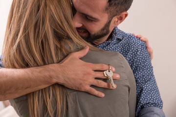 Young couple hug each other very happy because they have just bought a house, the man has the keys...