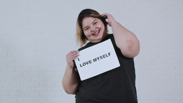 Concept body positivity - a chubby smiling woman dancing and holds a sign with the inscription I LOVE MYSELF