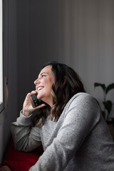 woman talks on the phone, young woman talks on the phone and smiles while looking out the window