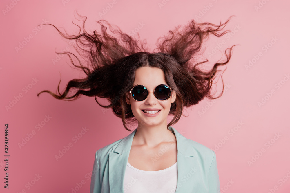 Wall mural Joyful excited surprised young woman with flying hair wear blazer sunglass on pink wall