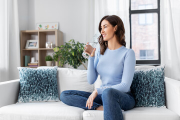 people, sustainability and leisure concept - happy smiling young woman drinking water from glass bottle at home