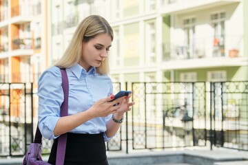 Young businesswoman with smartphone, street office building background