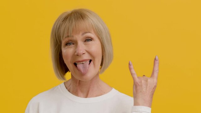 Mature rock lover. Playful positive middle aged lady showing punk gesture and sticking tongue out, feeling excited