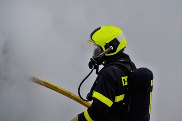 Naklejka premium A firefighter in a helmet and with a breathing apparatus is shrouded in smoke holding a hose during firefighting 