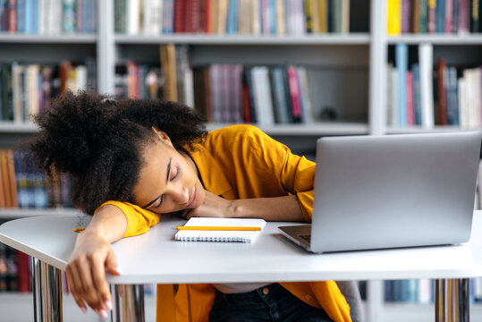 A tired sleepy African American female student fell asleep at a table during a lecture at a college. The girl is resting from study, closing her eyes and relaxing at her desk