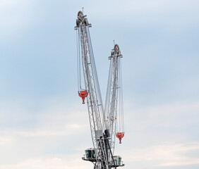 Two industrial cranes for building construction or weight lifting at sky background