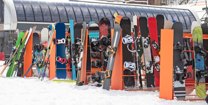 Alpine Skis And Snowboards Leaning On Ski Rack On Snow At Winter Day