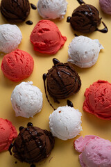 Various gelato scoops with chocolate sauce close up on golden surface