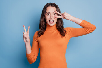 Fototapeta premium Photo of excited cheerful friendly woman on a blue background showing victory sign cover eye