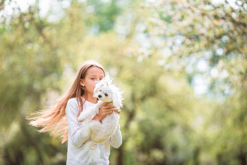 Naklejka premium Little smiling girl playing and hugging puppy in the park