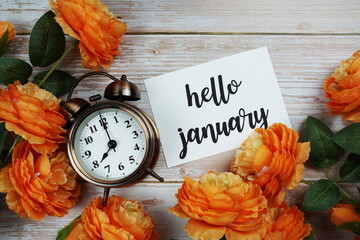 Hello January card and alarm clock with orange flower decoration on wooden background © may1985