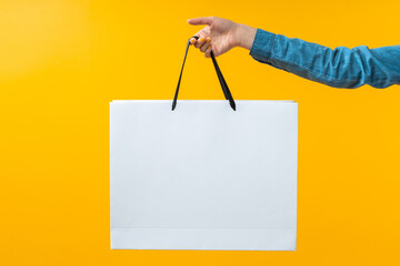 Close up cropped shot of female hand holding plain white shopping bag on bright colored yellow background - 429177429