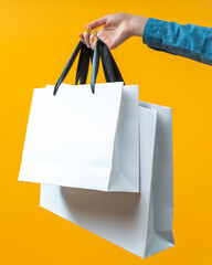 Vertical shot of female hand holding two blank white paper bags for shopping isolated over bright...