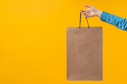 Studio photo of woman hand holding craft paper bag isolated on yellow background