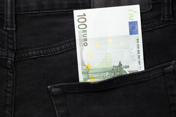 One hundred euro bill sticking out of the pocket of black jeans