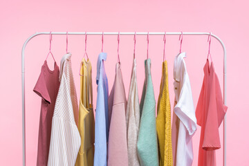 Collection of pastel colored women clothes hanging on rack in dressing room isolated on pink background - 429178623