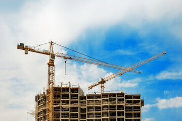 Two construction cranes against a blue sky background. Construction tower crane in yellow colour. Construction of a new building.